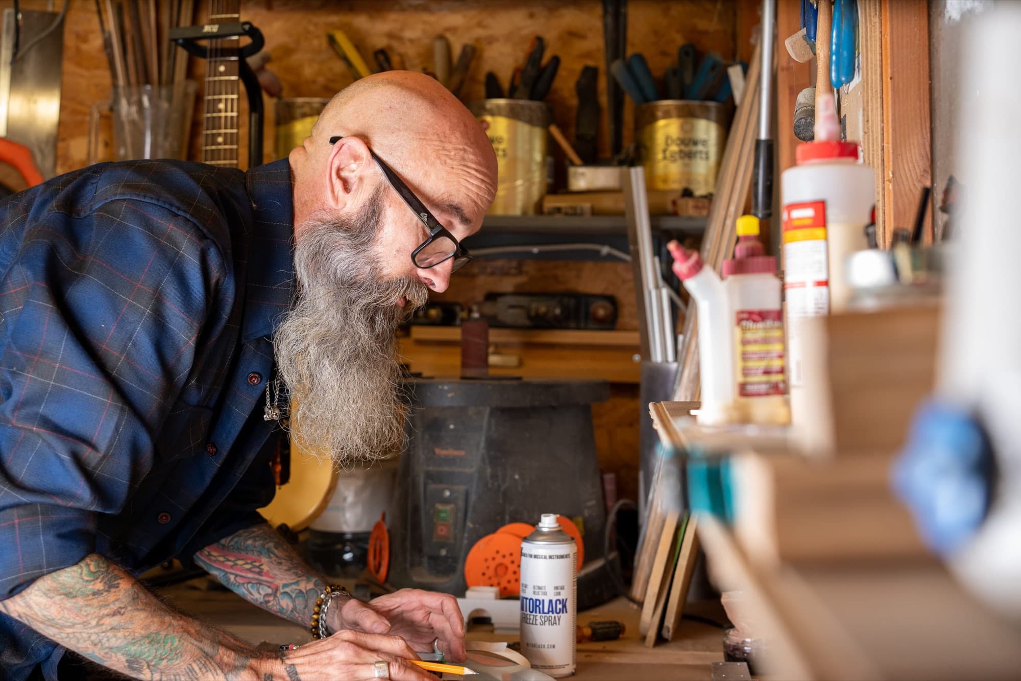 John leaning over his workbench, tools and tins on the shelves behind
